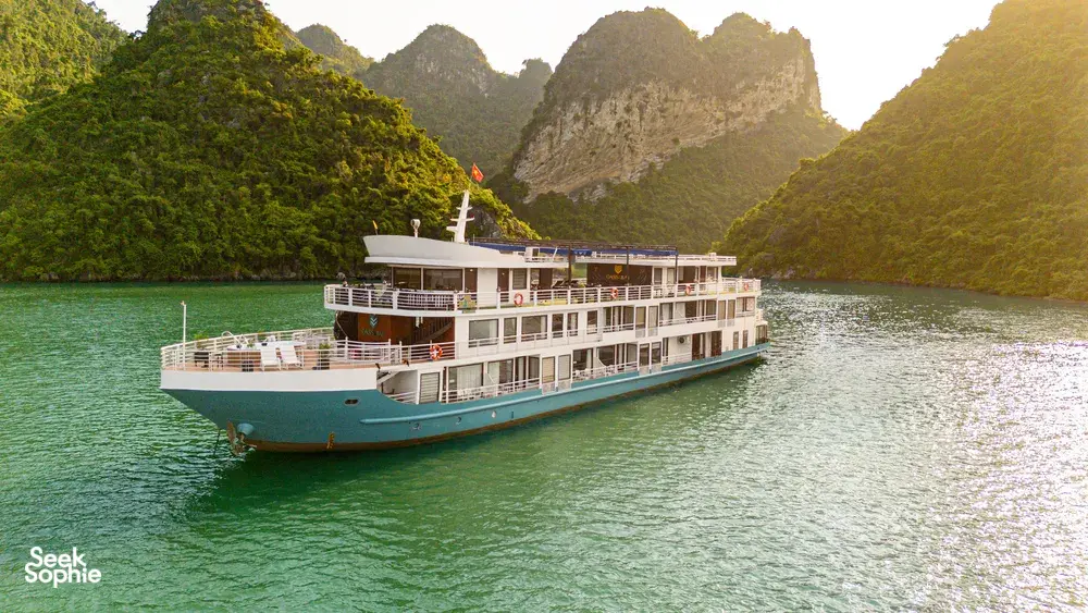 Oasis Bay party cruiser on Halong Bay in daylight, cruising past steep green karst mountains across calm emerald water