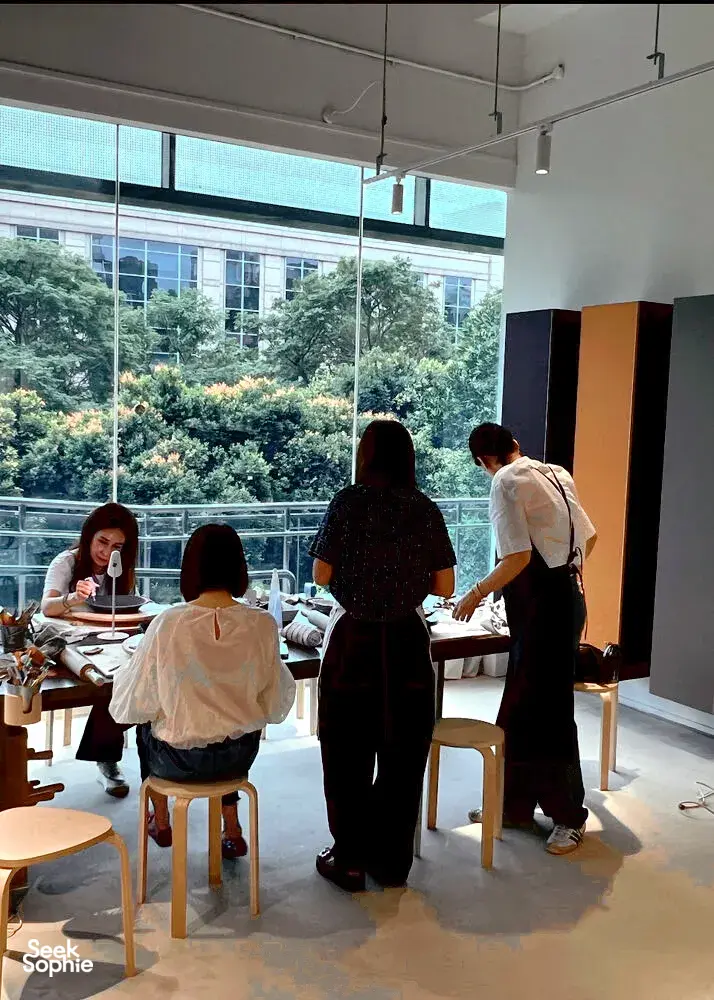 Tetamu di studio tembikar Singapura menghasilkan pinggan gaya Eropah antik di meja seramik, diterangi cahaya lembut dari tingkap besar