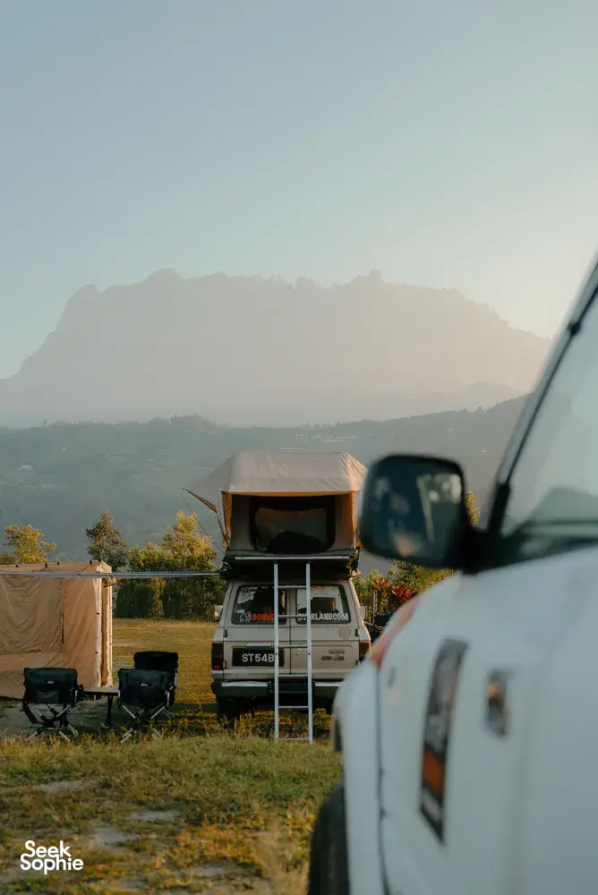 Borneo Overland wild roadtrip campsite near Kota Kinabalu with vans parked and hazy Mt Kinabalu in the distance