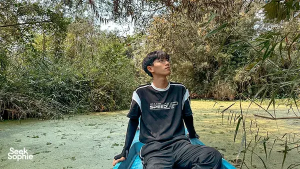 Traveller sitting cross-legged on a small boat on calm muddy water in the Mekong Delta, surrounded by reeds