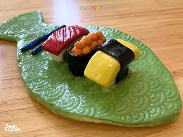 Green leaf-shaped ceramic platter on a wooden table, with tiny coloured clay pieces made during a 2-in-1 class workshops in Singapore