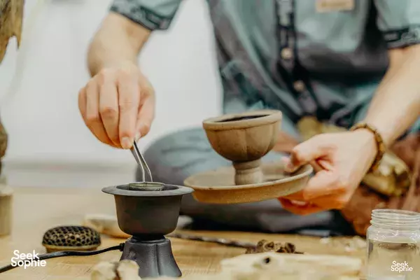 Hands pouring dark tea from a small pot into cups on a wooden table in Hanoi during a rare agarwood tour