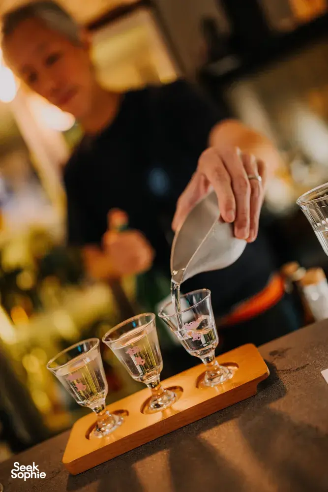 Rare sake tasting in a tucked-away shop in Singapore, SakeMama pours into small glasses on a wooden tray — date ideas Singapore