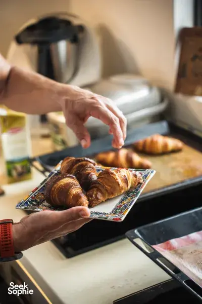 Hands place buttery croissants on a baking tray beside a stand mixer during a French Cooking Lab croissant workshop in Singapore