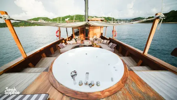 Circular jacuzzi on the wooden deck of a phinisi sailing past the coastline on a Komodo luxe cruise in Labuan Bajo