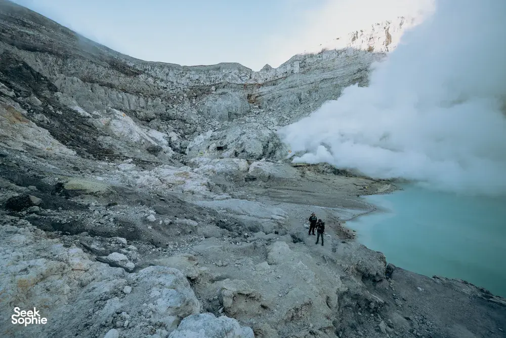 Hikers on the rocky rim of Mt Ijen at sunrise, watching the blue crater lake vents, on a 3D2N trip from Banyuwangi