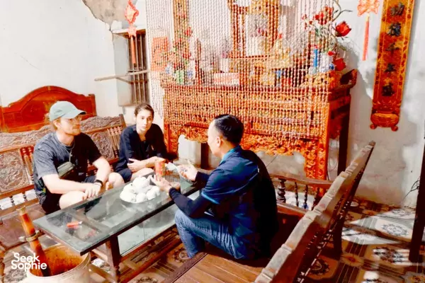 Travellers seated indoors with a host at a wooden tea table in Lovely Village Homestay in Ninh Binh during the 2D1N stay
