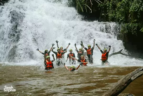 Group in orange life jackets splashing at the base of Dantala Waterfall in Da Lat during a waterfall experience