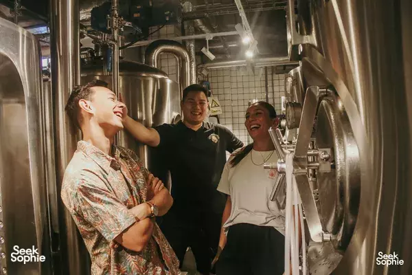 Friends smiling beside stainless fermentation tanks at Lion Brewery Co brewpub in Singapore, enjoying a craft beer tour