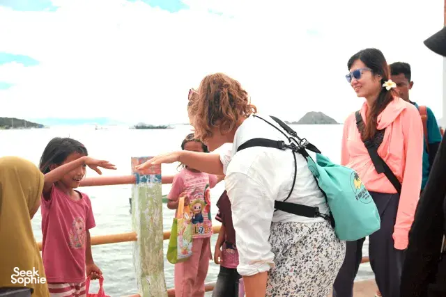 Tour group in life jackets leaning on a boat rail and waving while travelling across the water, Rinca day trip in Labuan Bajo