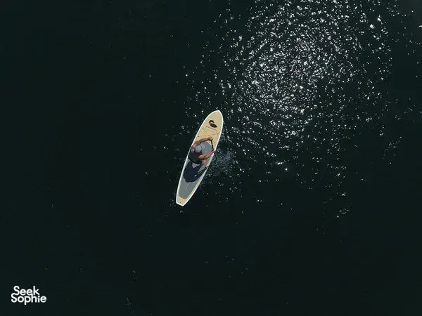 Top-down view of an SUP paddler gliding on dark ocean water at Tanjung Aru, Kota Kinabalu during sunrise