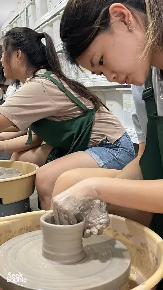 Pottery wheel lesson at 3Arts Pottery in Joo Chiat Place, Singapore, as students shape clay in green aprons — workshops in Singapore