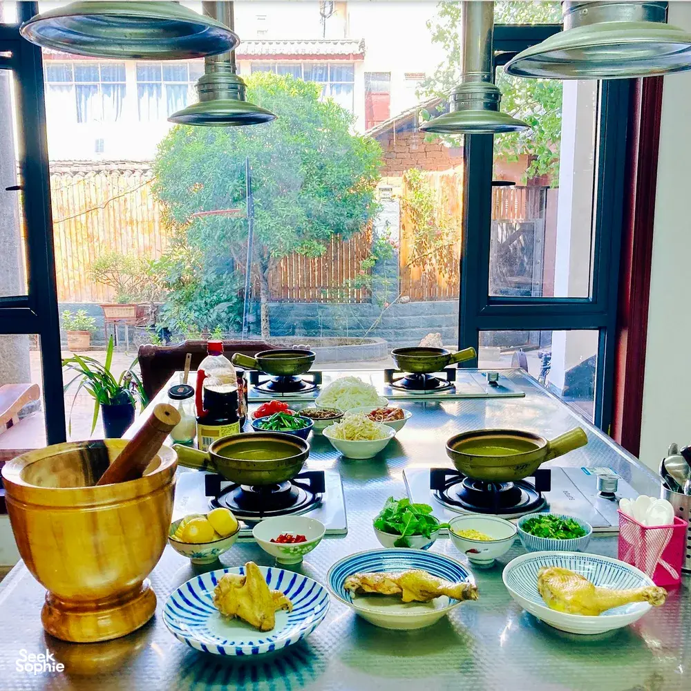 Cooking spread on stoves and table by a window in Lijiang, with pots of ingredients ready for a shared Yunnan meal