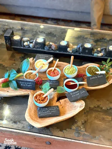Chalk-labeled bowls of edible-plant dips and sauces on a wooden board, set for bread making in Singapore hidden gems