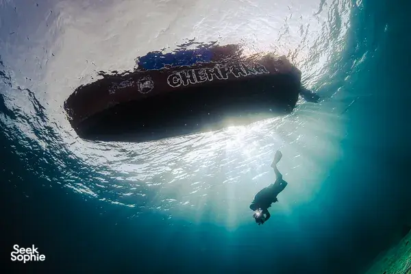 Diver silhouetted beneath a submerged shipwreck during a scuba dive, seen in Semporna’s clear ocean water