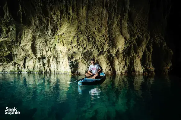 Kayaker glides across dark turquoise water inside a limestone cave in Phong Nha, Vietnam during a guided paddle