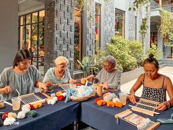 Thai weaving workshop at Kalm Village in Chiang Mai: participants work on small looms across a shared table of yarn