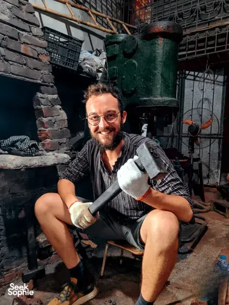 Man forging a knife with a hammer in a blacksmith workshop in Hanoi’s historic village, session led with Thanh