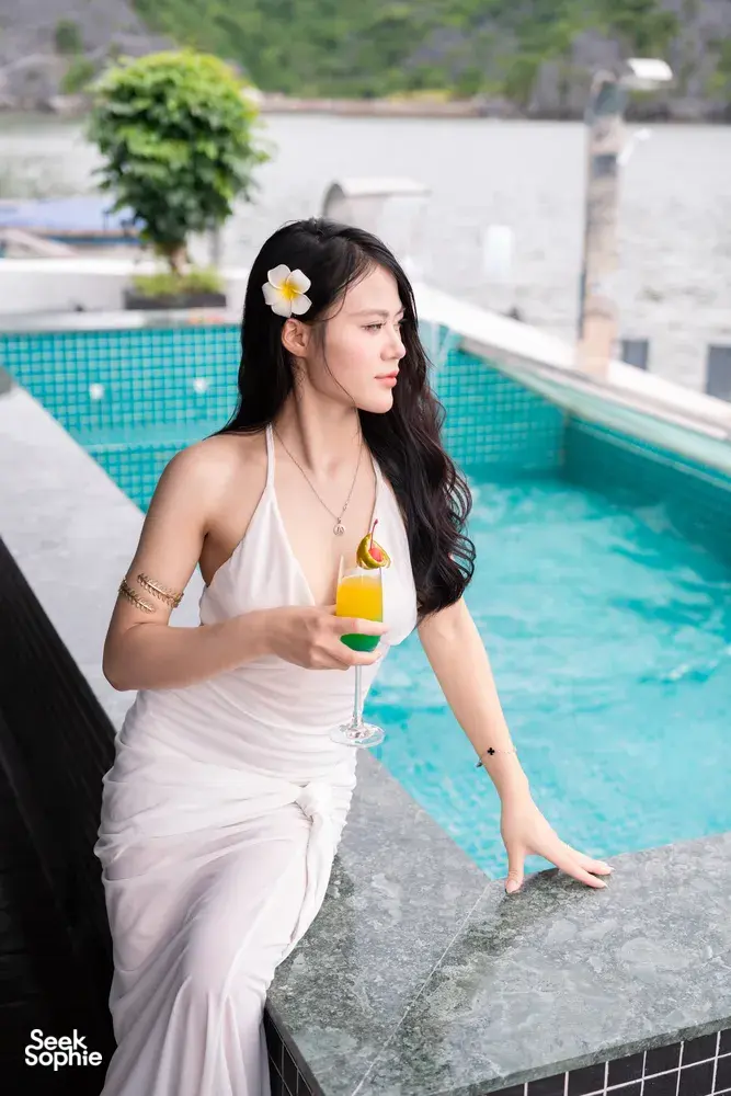Woman holding a cocktail beside the infinity-style pool on a luxe Cat Ba cruise, wearing a white dress with hair flower