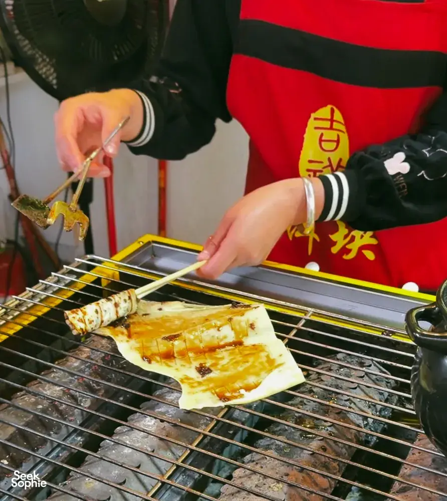 Grilled skewers on a street grill, served by a vendor in Lijiang during a food hunt with local stories
