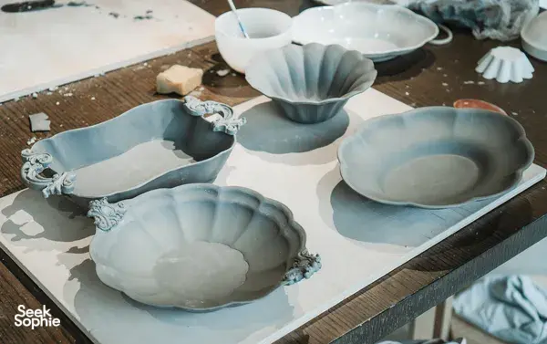 Light blue ceramic plates and shallow bowls with scalloped edges arranged on a pottery worktable at Ina Atelier workshops in Singapore