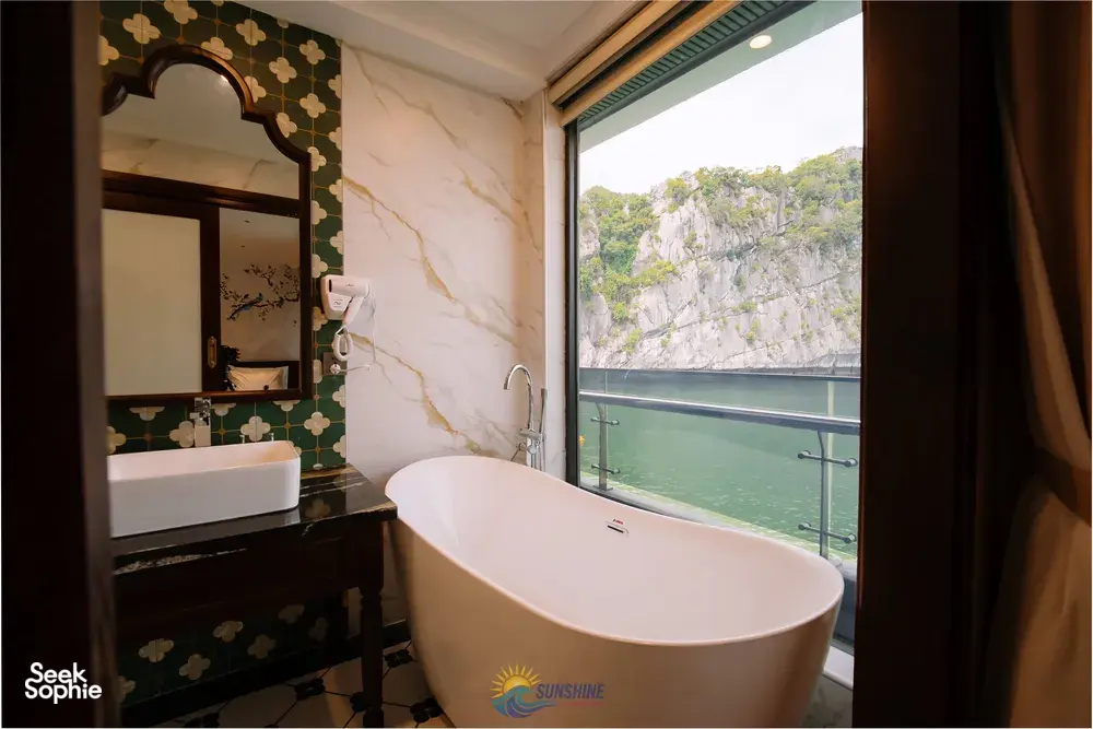 Freestanding bathtub in the ensuite of a Sunshine Golden Cruises suite, with a window view over Cat Ba waters