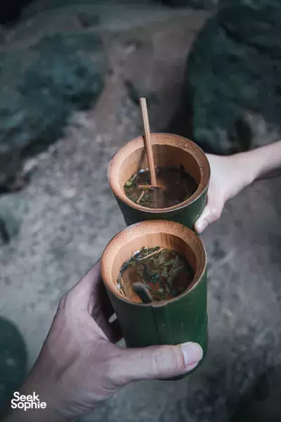 Bamboo cups of herbal drink clink in someone's hands during jungle dining at the eco-retreat, Khao Sok National Park