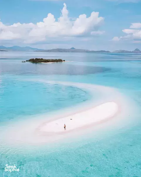 Overhead view of a tiny figure walking along a white sand spit surrounded by clear blue water near Labuan Bajo on Komodo Island
