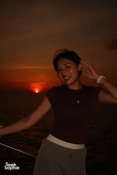 Seorang wanita tersenyum di dek saat matahari terbenam di atas laut lepas dalam pelayaran kapal pesiar pribadi saat matahari terbenam selama 3 jam dari Kota Kinabalu, Sabah