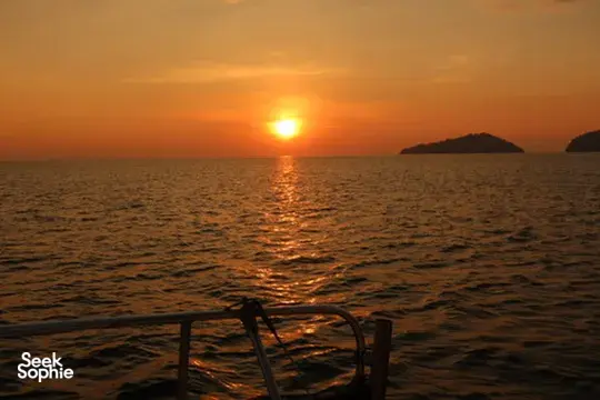 Matahari terbenam di atas laut yang tenang dengan pagar kapal pesiar di latar depan saat pelayaran matahari terbenam pribadi dari Kota Kinabalu, Sabah