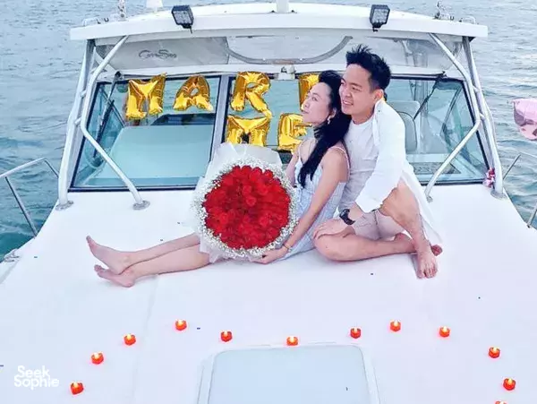 A couple pose on a yacht deck beside a red rose bouquet under MR & MRS balloons for date ideas Singapore