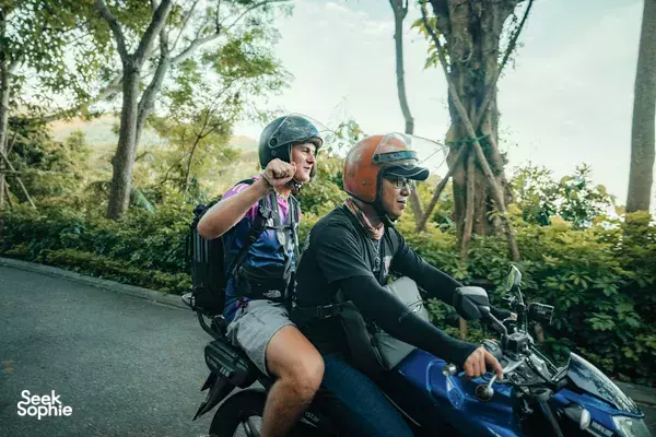 Two motorbike riders in helmets on a forest road in Da Nang, pausing for a wildlife-spotting stop during the ride