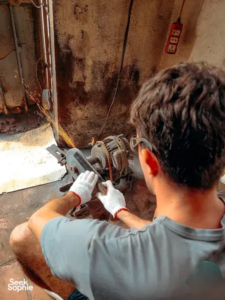 Back view of a participant hammering a hot knife blade on an anvil during the hands-on Hanoi blacksmith workshop experience