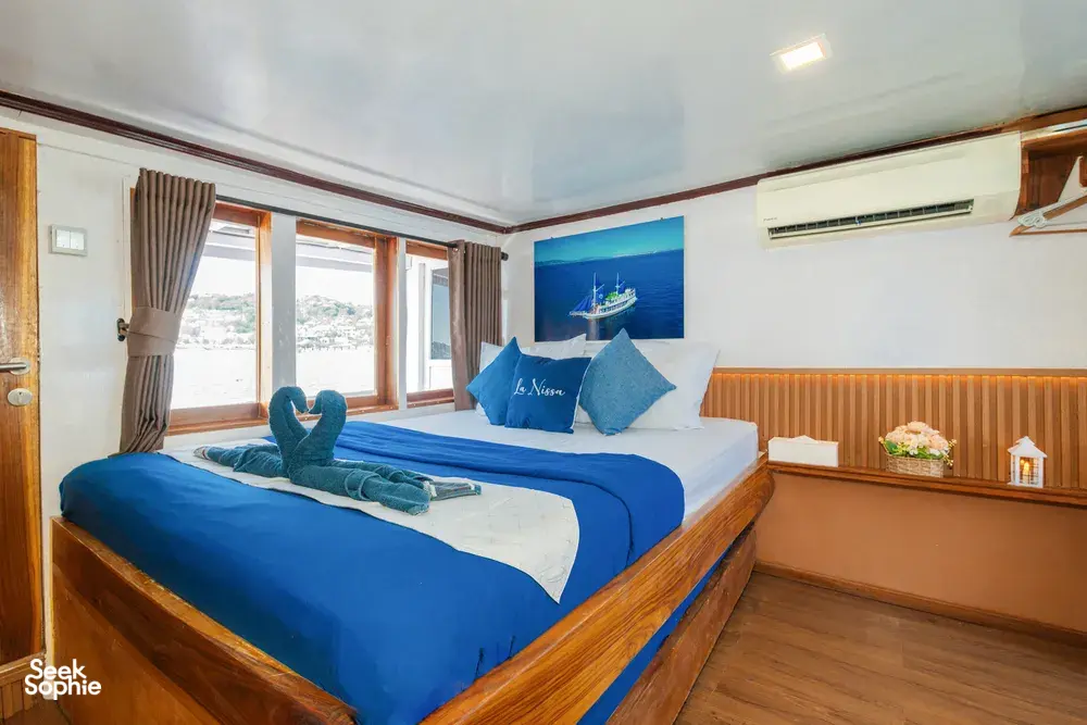 La Famille cabin on a Komodo boat with folded towel swan on blue bedding and sea view through the windows, Labuan Bajo