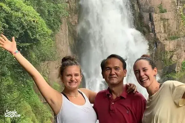 Travellers smiling and posing beside a roaring waterfall in Khao Yai National Park during a wildlife day trip