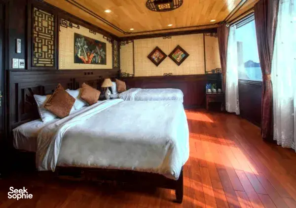 Cat Ba Ocean Cruises cabin with a double bed, patterned cushions and big window curtains, cosy space for a Cat Ba cruise