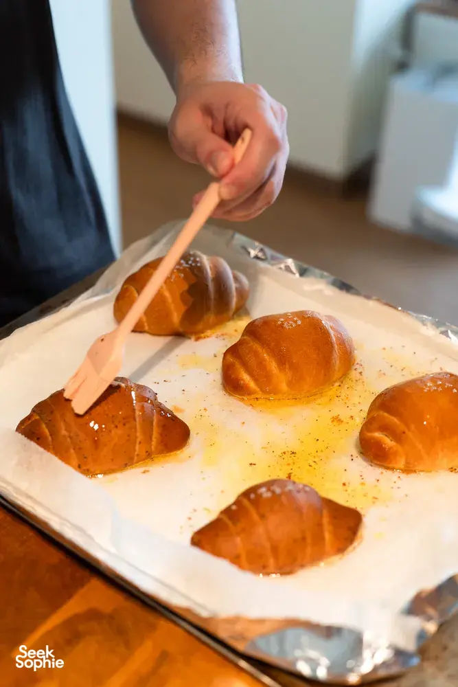 Hand using a brush to glaze shio pan buns on a parchment tray before baking—workshops in Singapore