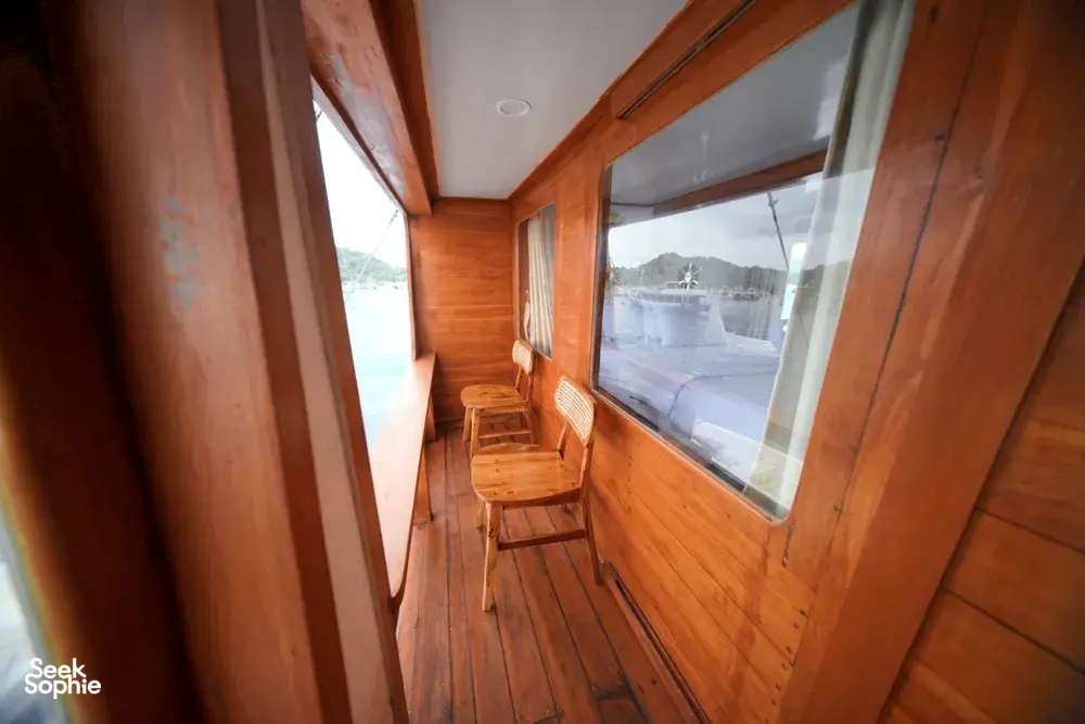 Wooden corridor with chair seating by large windows on a boat for a join-in 3D2N Komodo trip, near Komodo Island