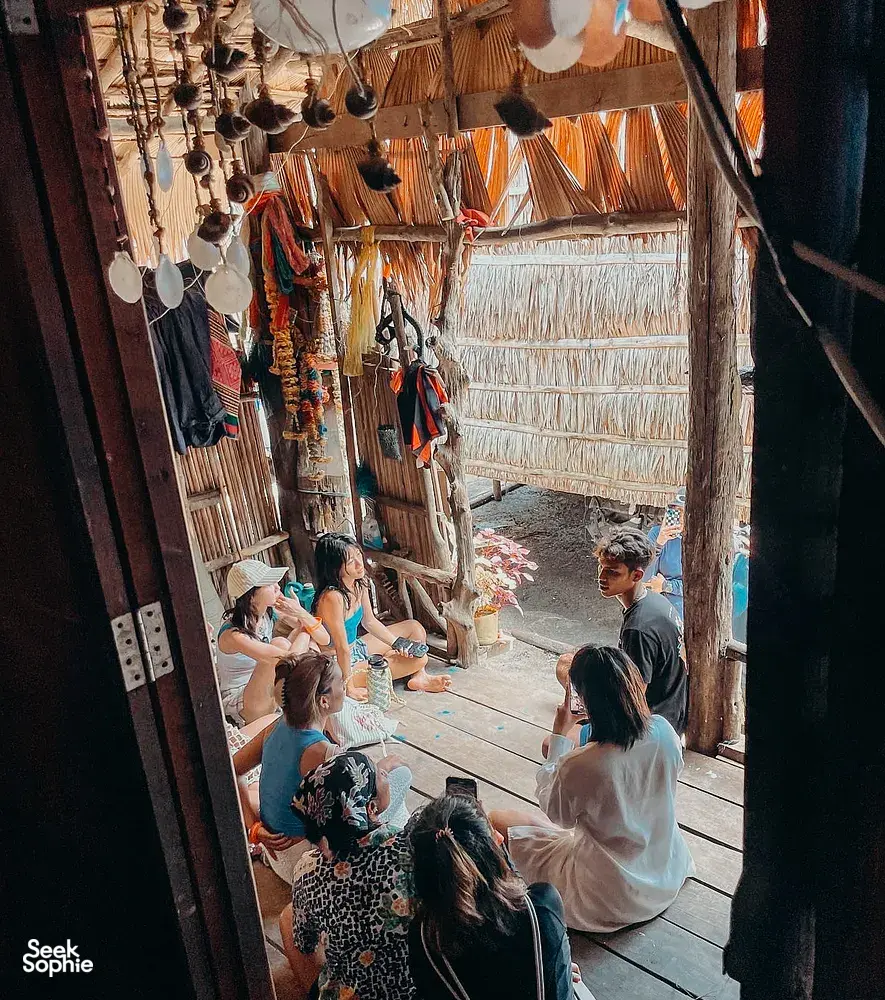 Group dining and chatting inside a thatched Moken-style hut during a Surin Island beach camping stay near Khao Lak