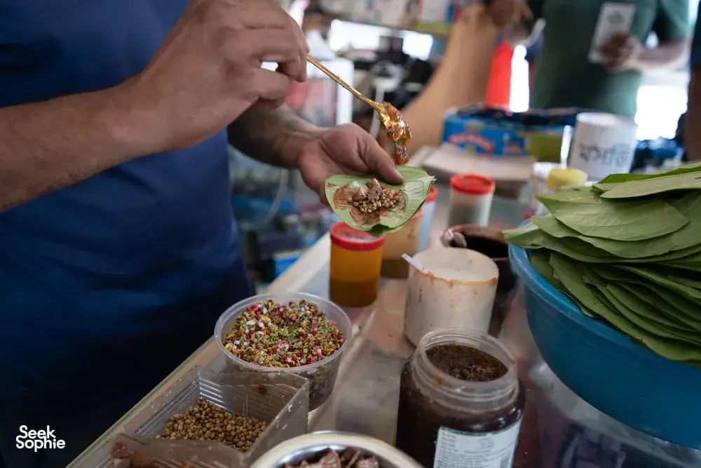 Hands preparing food at a table of spice trays and banana leaves during a Secrets of the Streets visit, Singapore hidden gems
