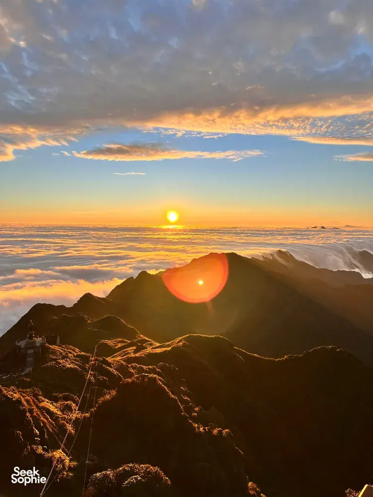 Golden sunrise from a mountain ridge above Sapa, with winding paths and ridgeline haze glowing at Mt Fansipan