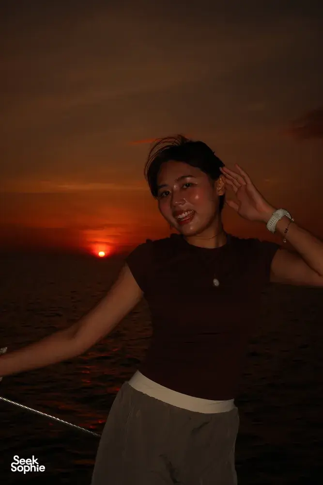 Seorang wanita tersenyum di atas dek ketika matahari terbenam di perairan terbuka semasa pelayaran kapal layar persendirian saat matahari terbenam selama 3 jam dari Kota Kinabalu, Sabah