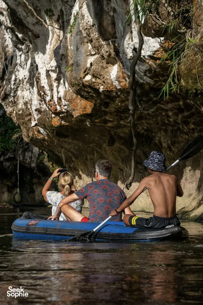 Family seated on an inflatable raft in dark lake water, drifting near rock walls at Khao Sok