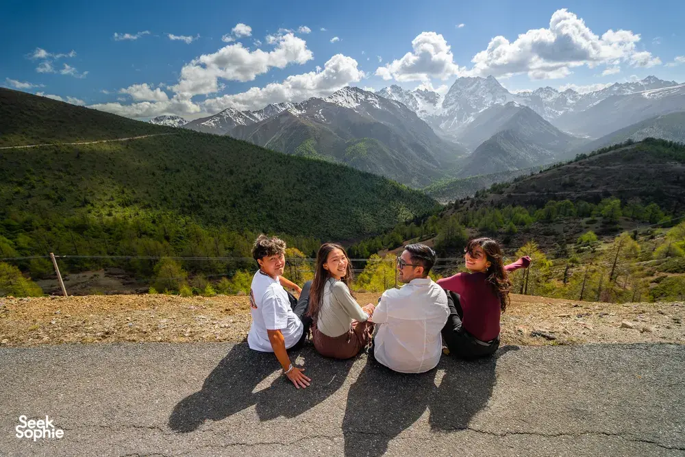 Travellers taking a break at a mountain overlook above Shangri-La, facing valleys on a 6-day trek with a Tibetan guide