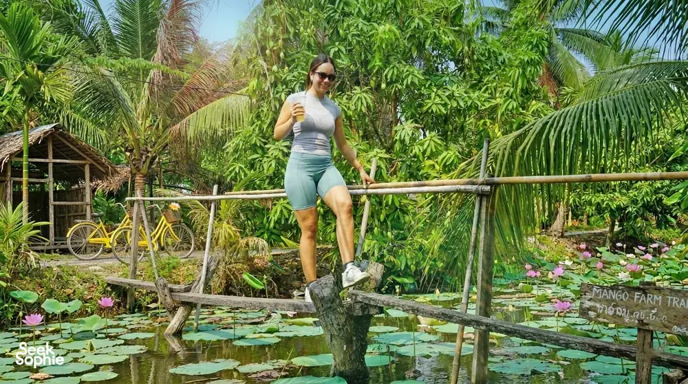 Traveller posing on a wooden bridge beside a lily pond on Mekong Island during a bike tour from Ho Chi Minh City