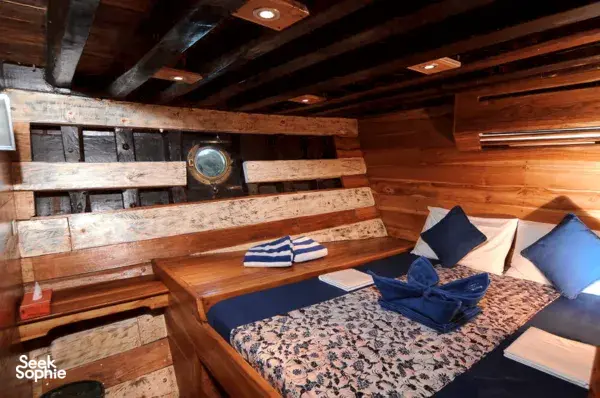Cozy bunk cabin with blue-and-white pillows and folded towels aboard the Moana Dive liveaboard for Komodo Island