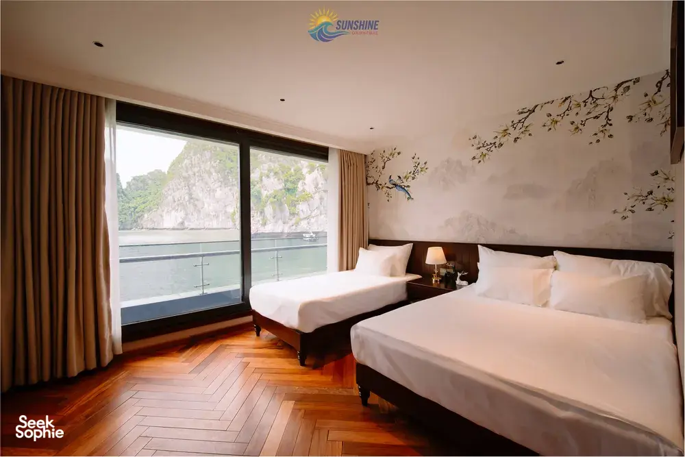 Sunshine Golden Cruises suite cabin with two beds and wide window framing limestone cliffs on a Cat Ba 2D1N cruise