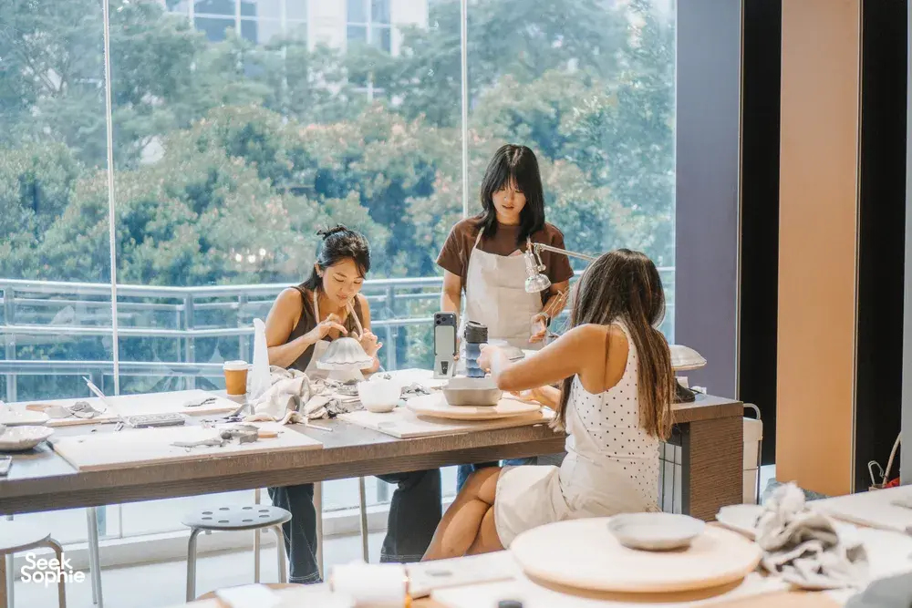Pottery workshop in a Singapore ceramics studio, participants handcrafting antique European-style plates at worktables by large windows