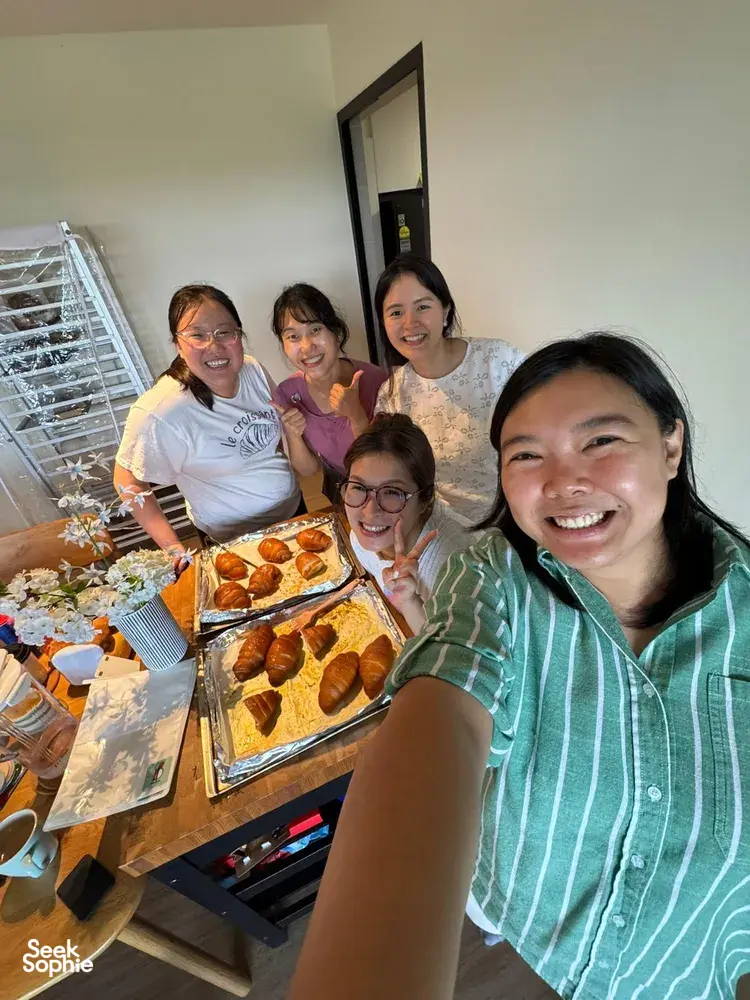 Smiling group beside a baking table of freshly baked pastries and trays in a kitchen during The Daily Staples workshops in Singapore