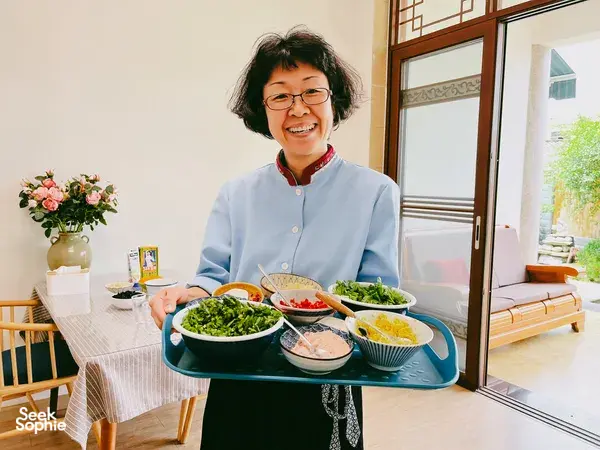 Fancy serving Yunnan dishes at a dining table in Lijiang during a market-to-table cooking experience, with bowls of greens